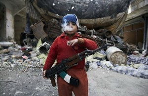 Ahmed a huit ans, fils d'un rebelle syrien pendant la guerre civile. Cet enfant monte la garde, AK-47 autour du cou, cigarette à la bouche dans les décombres de Alep (Syrie).